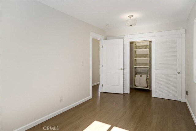 unfurnished bedroom with a closet, baseboards, and wood finished floors