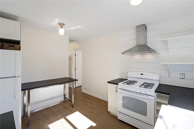 kitchen featuring dark countertops, wood finished floors, white appliances, wall chimney exhaust hood, and baseboards