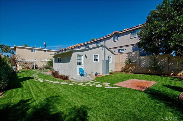 rear view of house featuring stucco siding, a yard, and fence