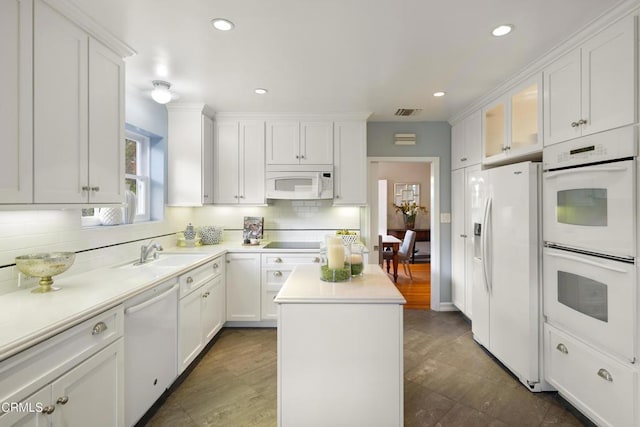 kitchen with white appliances, visible vents, a kitchen island, a sink, and white cabinetry