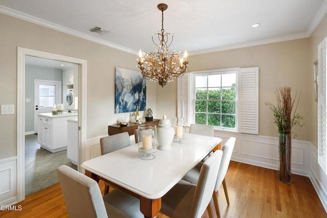 dining room with light wood finished floors, visible vents, stacked washer and clothes dryer, and wainscoting