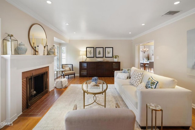 living room with visible vents, a chandelier, ornamental molding, a fireplace, and wood finished floors