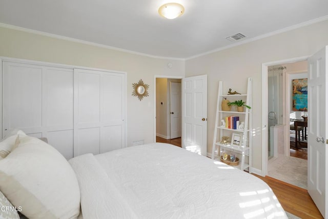 bedroom featuring visible vents, baseboards, ornamental molding, wood finished floors, and a closet