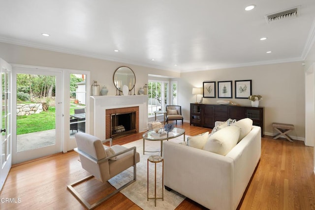 living room featuring light wood finished floors, visible vents, a brick fireplace, crown molding, and baseboards