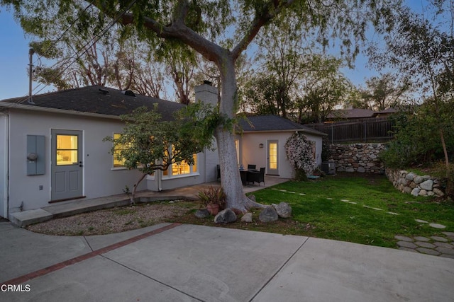 back of property featuring stucco siding, a lawn, fence, a chimney, and a patio area