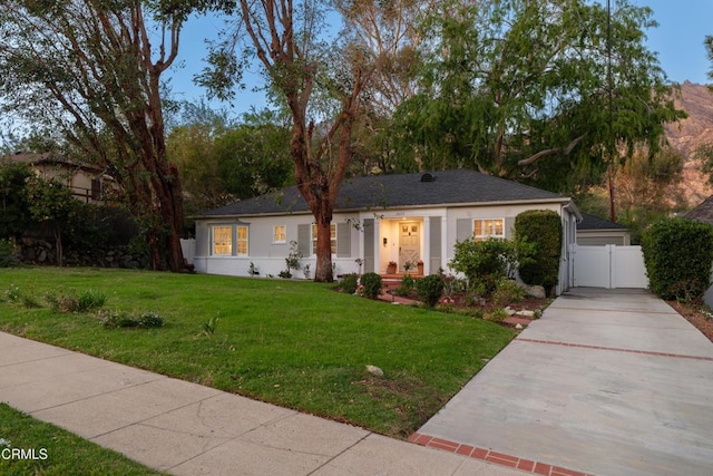 view of front facade featuring stucco siding, fence, a front yard, and a gate