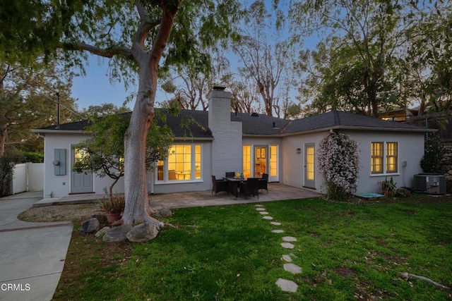 back of house featuring fence, a lawn, cooling unit, a chimney, and a patio