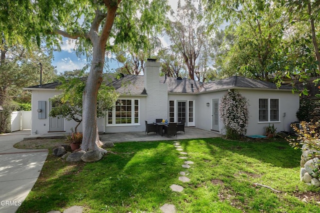 rear view of house with fence, a yard, stucco siding, a chimney, and a patio area