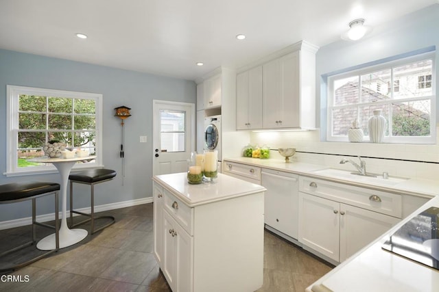 kitchen featuring stacked washer and clothes dryer, a sink, backsplash, white cabinetry, and white dishwasher