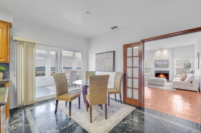 dining room featuring visible vents, marble finish floor, and a warm lit fireplace