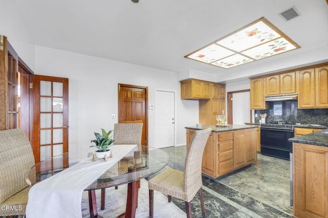 kitchen with visible vents, a kitchen island, under cabinet range hood, range with gas stovetop, and decorative backsplash