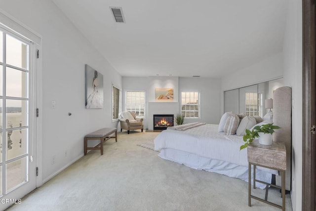 bedroom with a glass covered fireplace, baseboards, visible vents, and light carpet