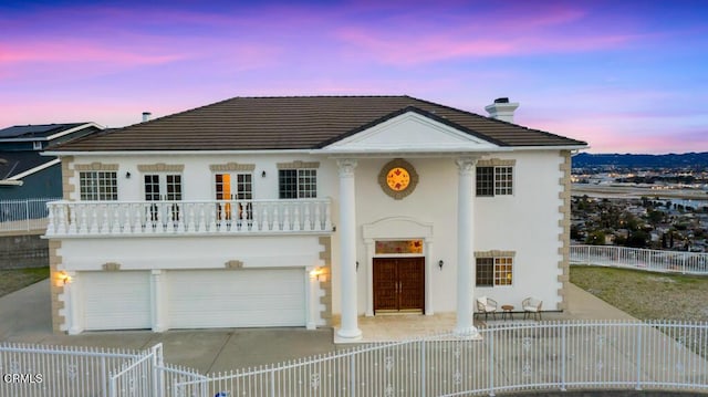 view of front of house with driveway, a fenced front yard, an attached garage, a balcony, and a chimney