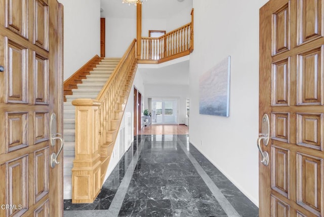 foyer entrance with stairs, baseboards, marble finish floor, and a towering ceiling