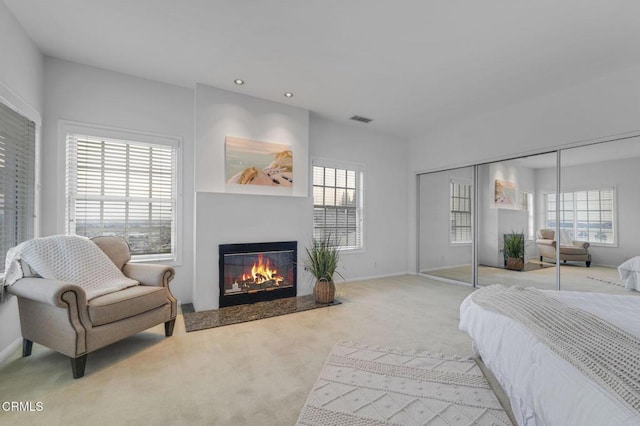 bedroom featuring a glass covered fireplace, multiple windows, carpet, and visible vents