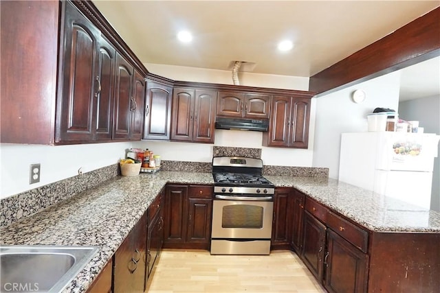 kitchen featuring light stone counters, light wood-style floors, gas range, under cabinet range hood, and freestanding refrigerator