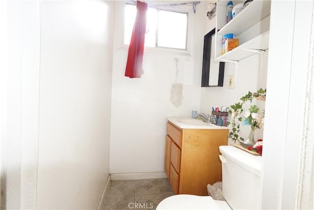 half bath with baseboards, vanity, and toilet