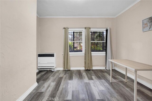 unfurnished dining area featuring heating unit, baseboards, crown molding, and wood finished floors