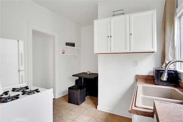 kitchen with light countertops, a sink, freestanding refrigerator, white cabinetry, and light tile patterned floors