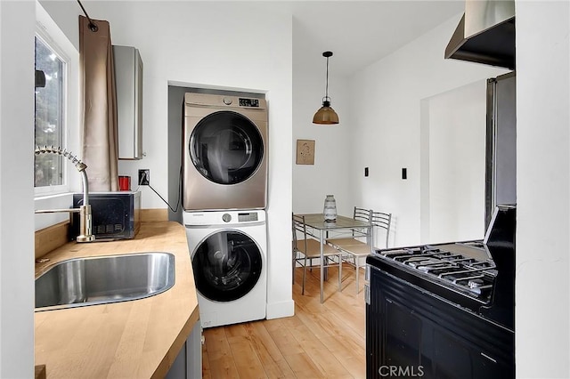 washroom featuring stacked washer and clothes dryer, a sink, laundry area, and light wood-style floors