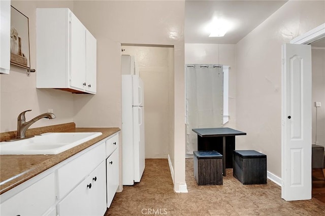 kitchen with freestanding refrigerator, white cabinets, and a sink