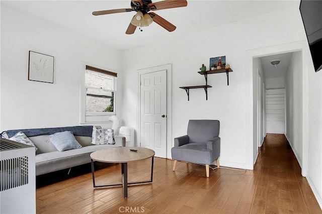 living area with baseboards, wood finished floors, and a ceiling fan