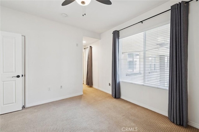 unfurnished room featuring a ceiling fan, baseboards, and light carpet