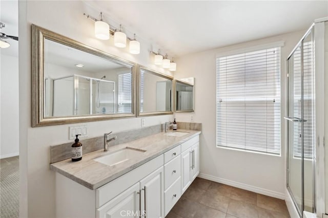 full bathroom featuring double vanity, a stall shower, baseboards, and a sink