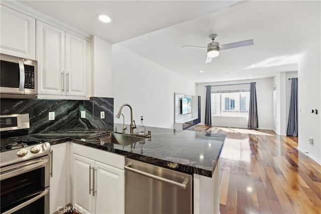 kitchen with tasteful backsplash, light wood-type flooring, appliances with stainless steel finishes, a peninsula, and white cabinets