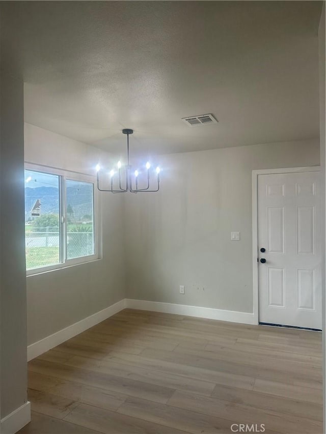 unfurnished dining area featuring an inviting chandelier, light wood-style floors, visible vents, and baseboards