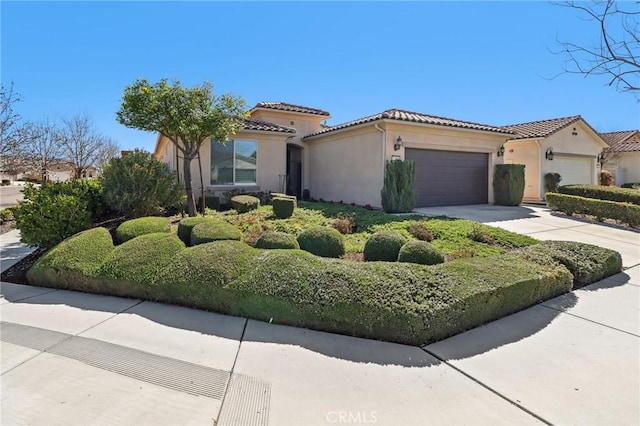 mediterranean / spanish-style home with stucco siding, concrete driveway, an attached garage, and a tiled roof