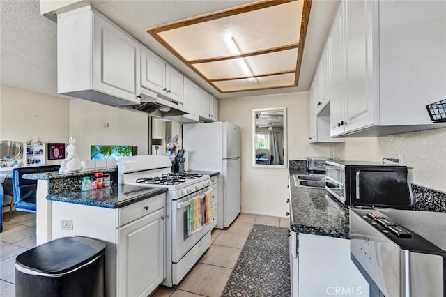 kitchen with under cabinet range hood, a peninsula, white cabinets, light tile patterned floors, and white range with gas stovetop