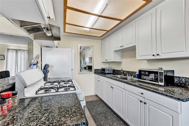 kitchen with a sink, white appliances, light tile patterned floors, and white cabinetry