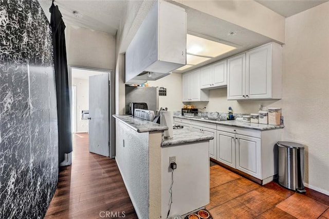 kitchen with dark wood finished floors, a peninsula, light stone counters, and white cabinetry