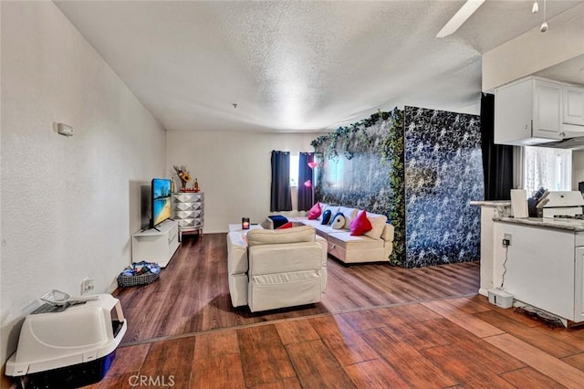 living area featuring a textured wall, a textured ceiling, a ceiling fan, and wood-type flooring