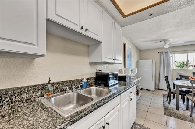 kitchen featuring dark countertops, black microwave, freestanding refrigerator, white cabinetry, and a sink