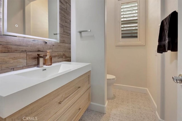 bathroom with wooden walls, toilet, vanity, and baseboards