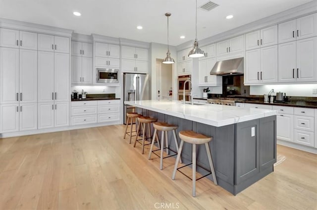 kitchen featuring light wood finished floors, visible vents, wall chimney range hood, appliances with stainless steel finishes, and a sink