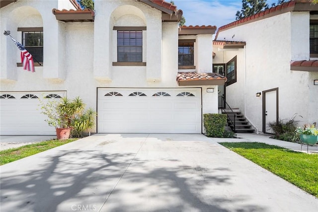 mediterranean / spanish-style house featuring an attached garage, a tile roof, and concrete driveway