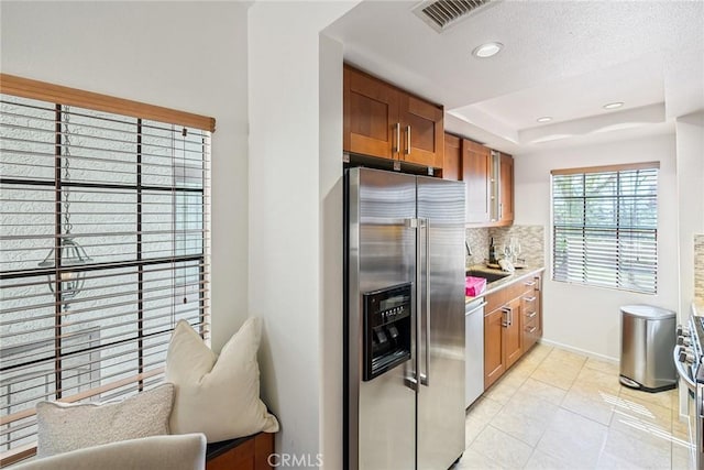 kitchen with visible vents, a tray ceiling, decorative backsplash, appliances with stainless steel finishes, and brown cabinets