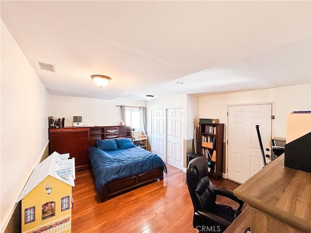 bedroom featuring wood finished floors, visible vents, a closet, and baseboards