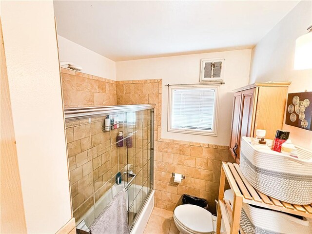 full bath featuring visible vents, shower / bath combination with glass door, wainscoting, tile walls, and toilet