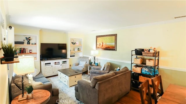 living area with built in features, crown molding, visible vents, and wood finished floors