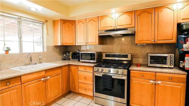 kitchen with under cabinet range hood, a sink, stainless steel appliances, a toaster, and decorative backsplash