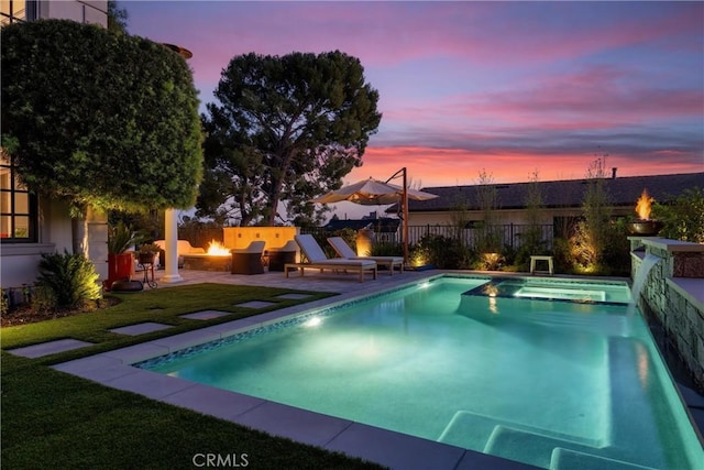 pool at dusk featuring fence, a fenced in pool, a fire pit, a patio area, and a lawn