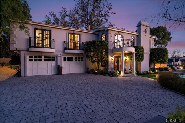 view of front of home featuring stucco siding, french doors, decorative driveway, a balcony, and a garage