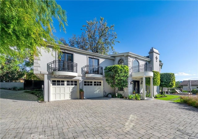 view of front of house with a balcony, an attached garage, a chimney, stucco siding, and decorative driveway