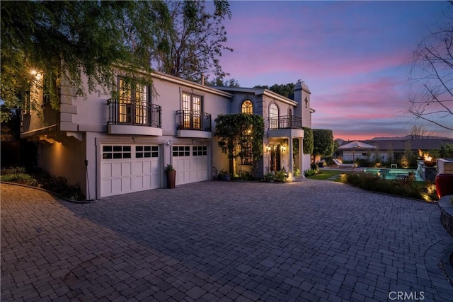 view of front of house featuring a balcony, an attached garage, a chimney, stucco siding, and decorative driveway