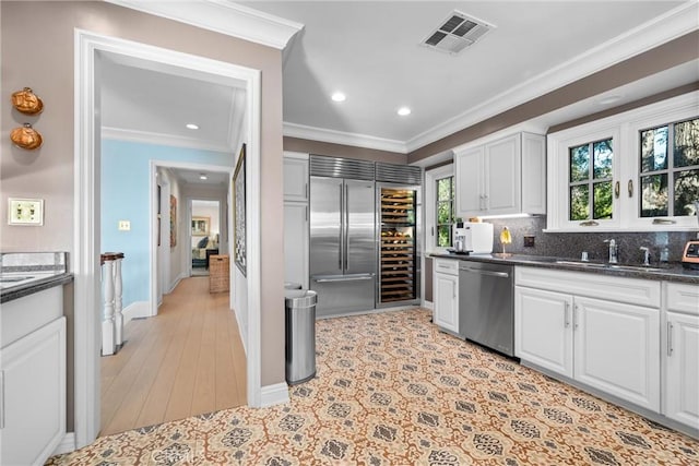 kitchen featuring visible vents, crown molding, stainless steel appliances, white cabinetry, and a sink