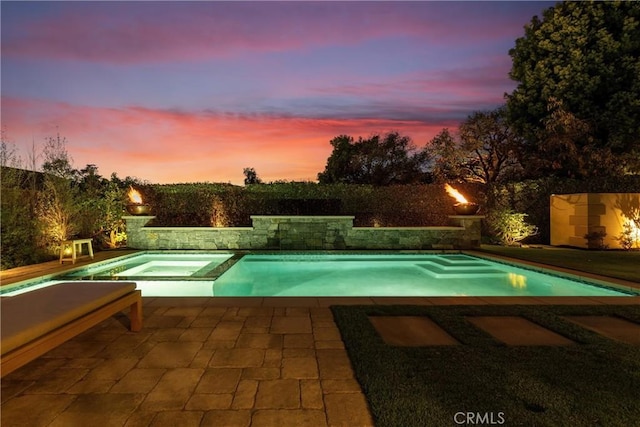 pool at dusk featuring a pool with connected hot tub and a patio area